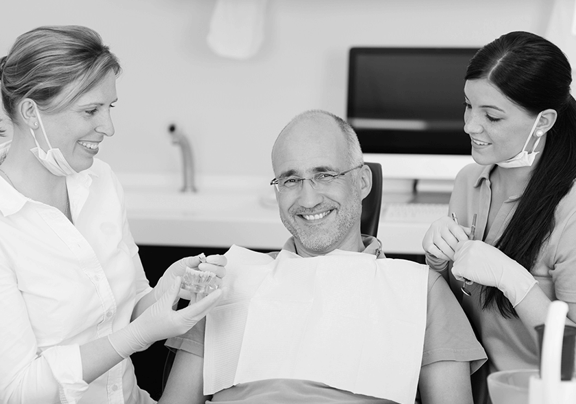 A patient smiling while being assisted by a dentist and dental assistant.